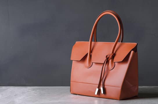 Tan leather handbag with rolled handles and a fold-over flap